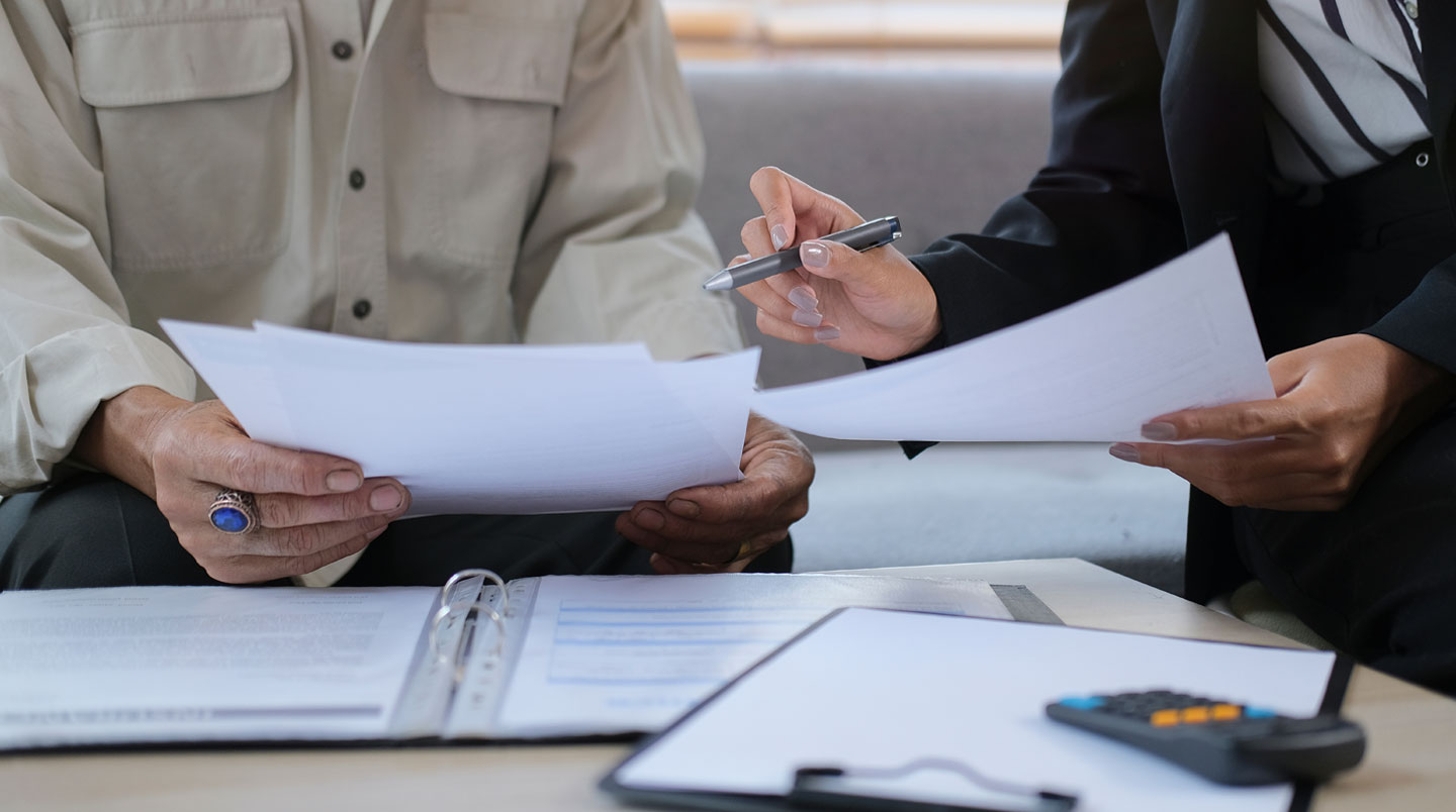 Mains âgées tenant un relevé bancaire français montrant un versement de pension de retraite CARSAT de 620€, calculatrice et notes manuscrites sur une table en bois, lumière naturelle